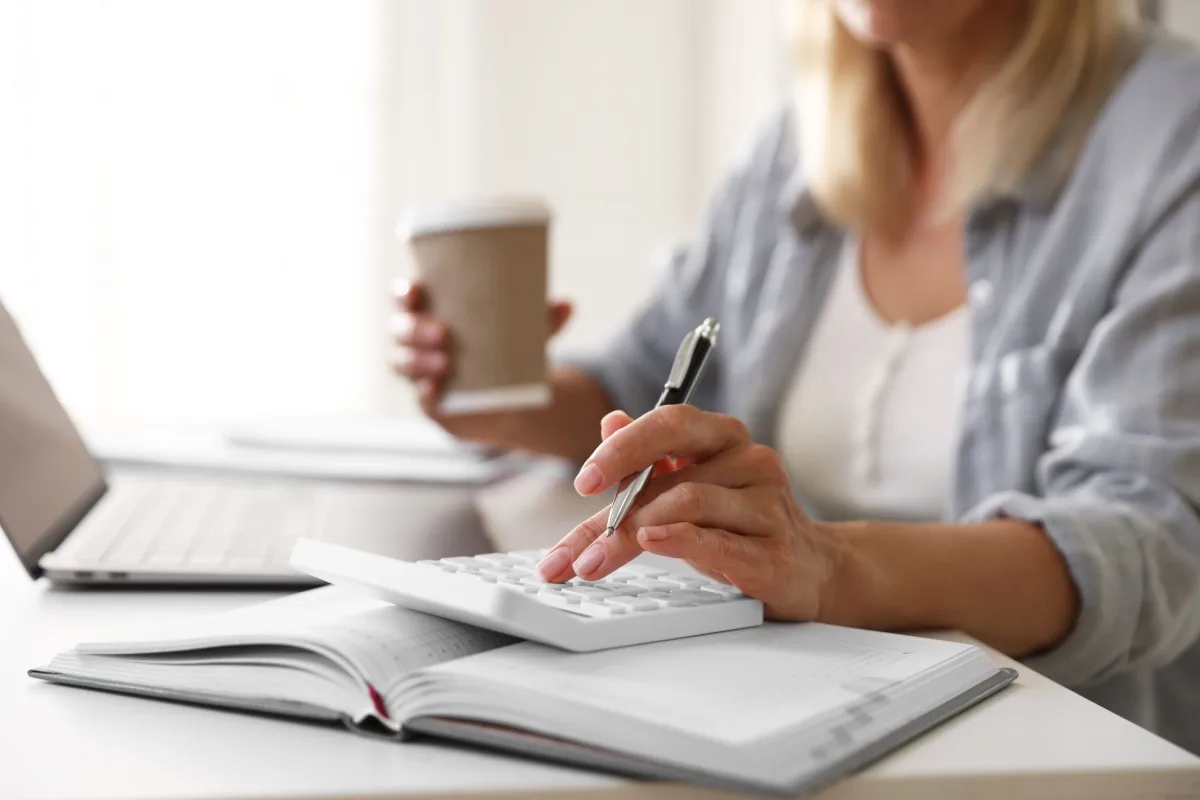 Woman using a calculator and holding a cup of coffee