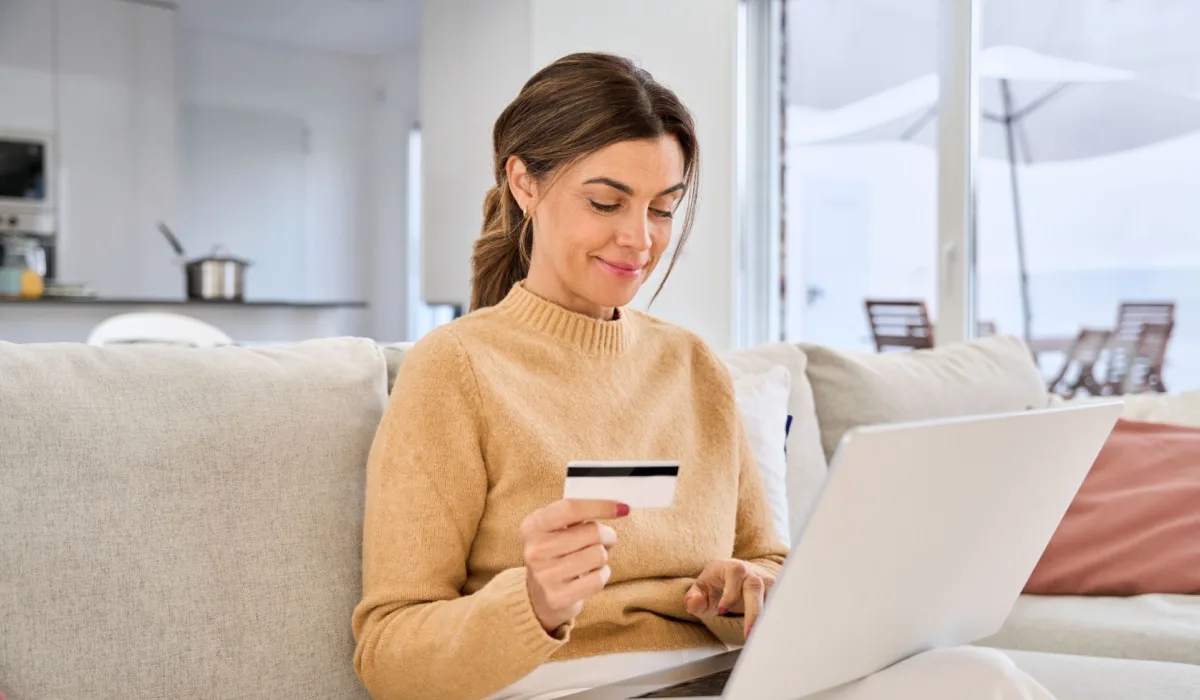 Happy middle-aged woman holding a credit card while shopping on a laptop