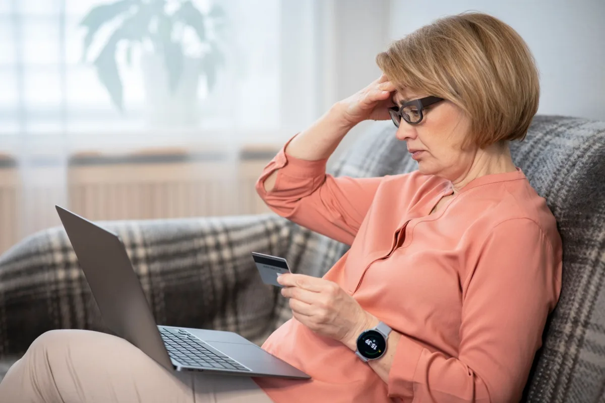 Stressed-looking middle-aged woman looking at her credit card and a laptop