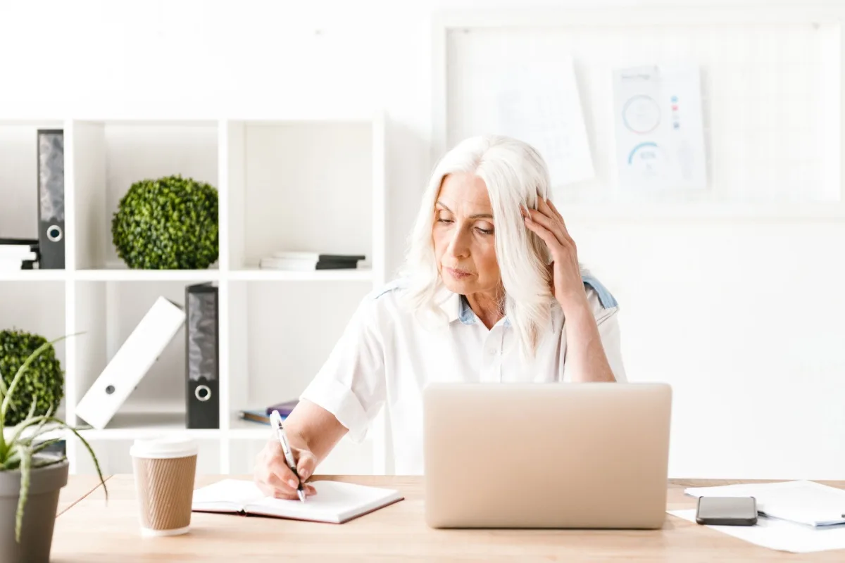 A mature woman learning at her laptop and taking notes