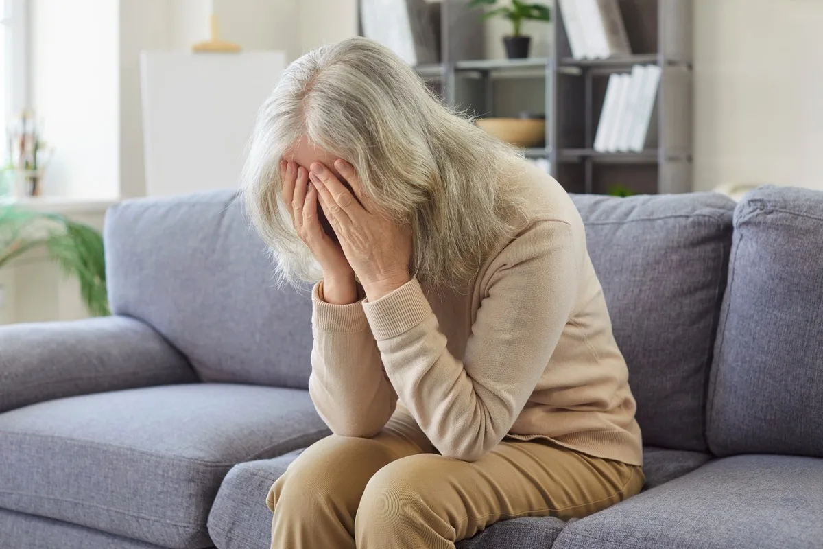An older woman on the sofa with her head in her hands